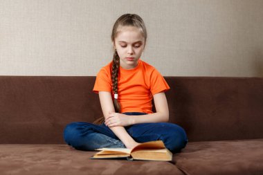 Portakal rengi tişört giyen, Lotus pozu veren, güzel, güzel, odaklanmış, neşeli genç bir kızın portresi.