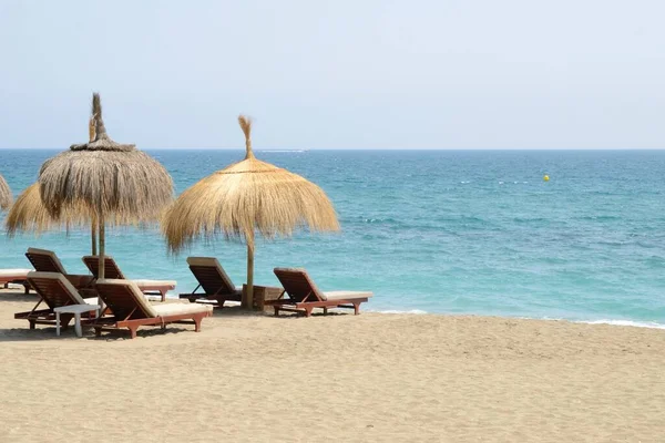 西班牙安达卢西亚马贝拉海滩岸边的太阳床和柳条雨伞 图库图片