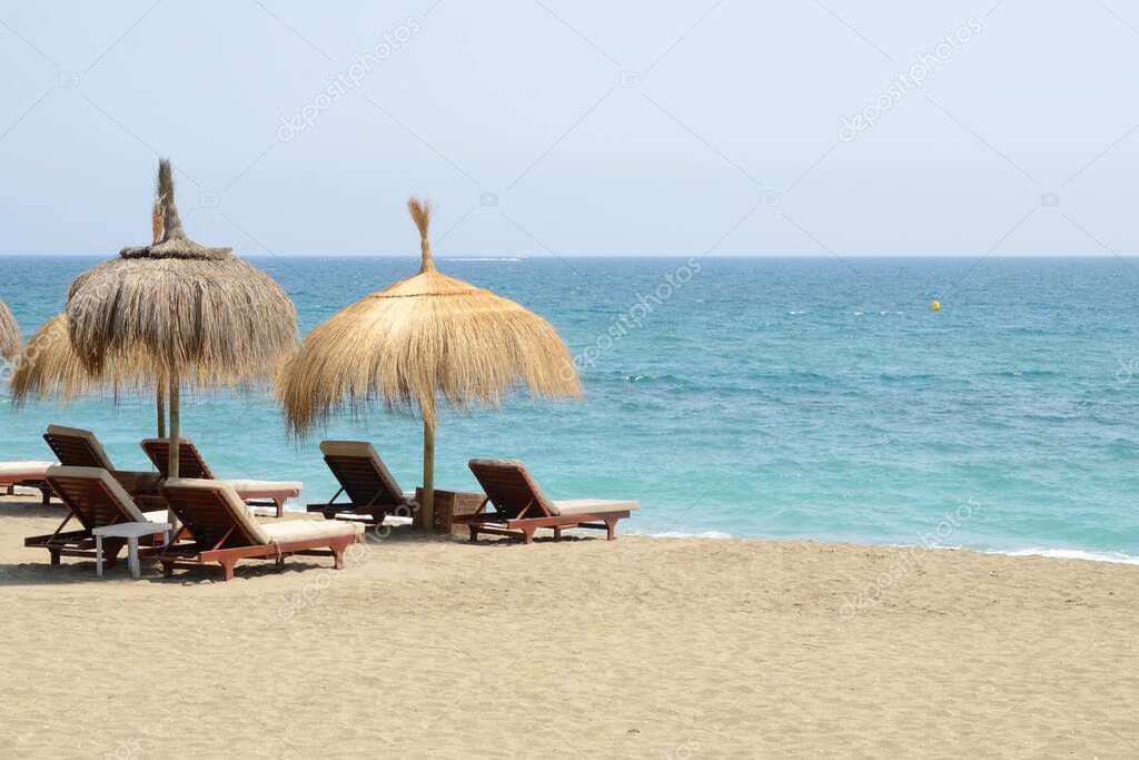 Sun beds and wicker umbrellas at the shore of the beach in Marbella, Andalusia, Spain