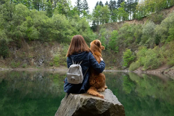 Девушка с собакой сидит на камне на озере. Женщина и животное . — стоковое фото