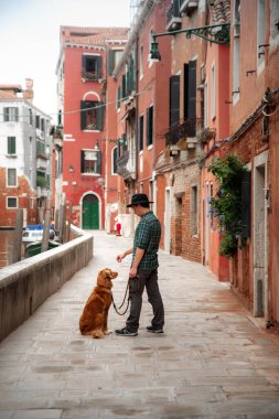 Venedik rıhtımında köpeği olan bir adam. Bir evcil hayvanla seyahat etmek. Nova Scotia Duck Tolling Retriever şehirde tasmalı