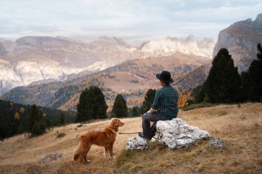 Dağlarda köpekli bir adam. Seyahat, evcil bir hayvanla yürüyüş. Nova Scotia Duck Tolling Retriever