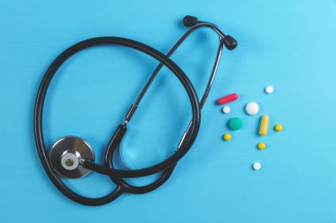 Stetoskop ve mavi arka planda çok renkli tabletler ve kapsüller. Üst görünüm
