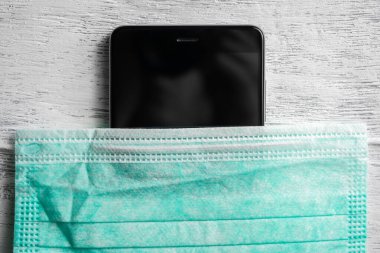 Tıbbi maskeli bir telefon. Akıllı telefonunuzu virüslerden koruyorum. Enfeksiyonların telefondan yayılması. Telefon aracılığıyla koronavirüs enfeksiyonu..