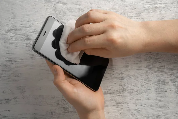 Male hands wiping the smartphone with alcohol-based disinfectant wipes to clean and prevent the spread of bacteria and viruses. Concept of personal hygiene and prevention of the spread of coronavirus infection