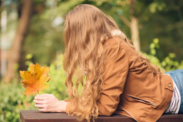 Beauté femme tenant des feuilles d'automne et relaxant un banc — Photo