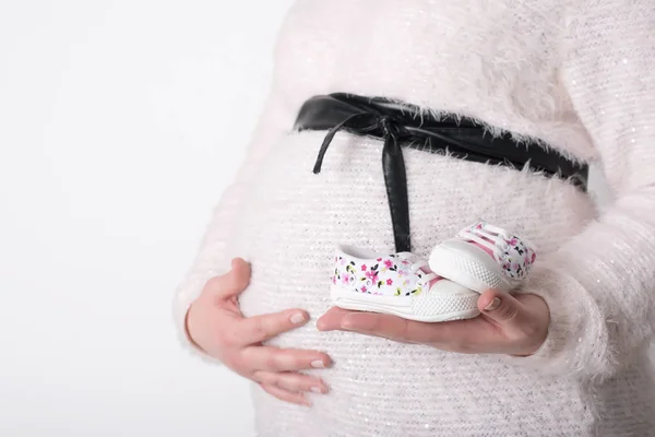 Foto de mujer embarazada sosteniendo zapatos de bebé —  Fotos de Stock