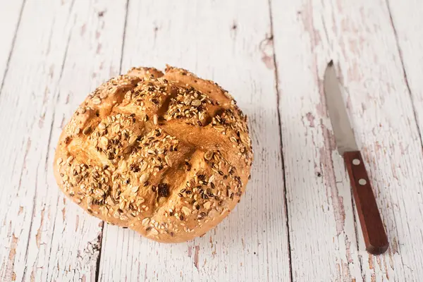 Fresh seedy bread with knife on a white wooden — Stock Photo, Image