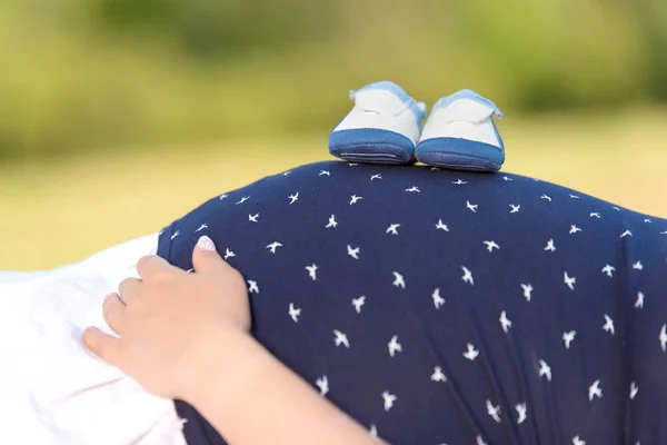 Foto de uma barriga grávida com sapatos de bebê — Fotografia de Stock