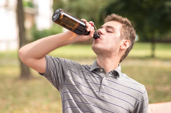 Junger Mann trinkt ein Bier im Park — Stockfoto