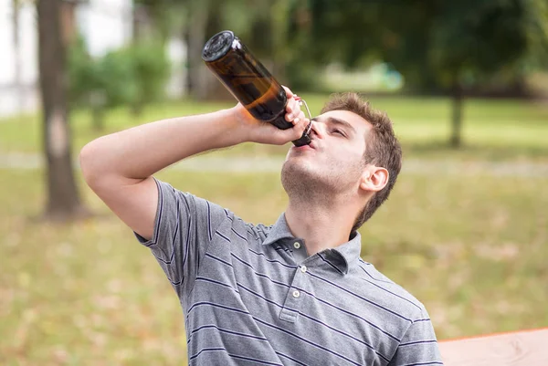 Young man drinking a beer in the park — Stock Photo, Image
