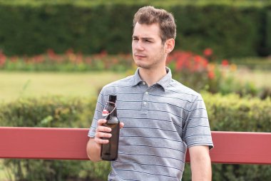 Bir şişe bira ile bankta oturan genç adam