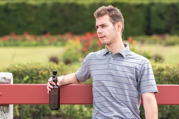 Junger Mann sitzt mit Bierflasche auf Bank — Stockfoto