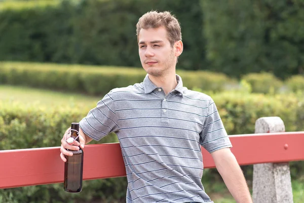 Junger Mann sitzt mit Bierflasche auf Bank — Stockfoto