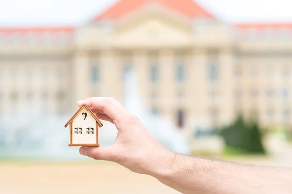 Man hand holding a wooden model house over the blur building