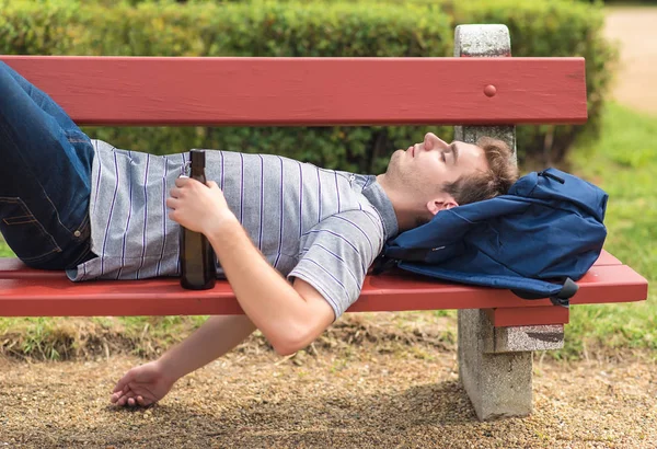 Junger Mann entspannt sich mit einer Flasche Bier auf einer Bank — Stockfoto