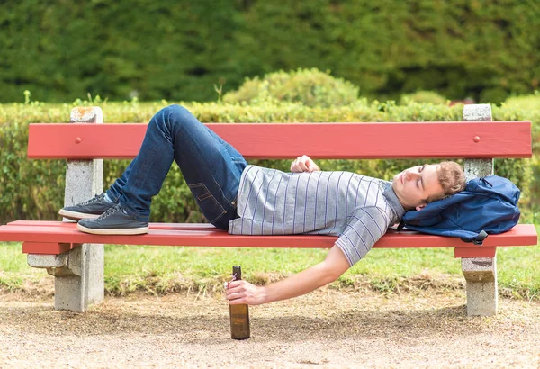 Junger Mann entspannt sich mit einer Flasche Bier auf einer Bank — Stockfoto