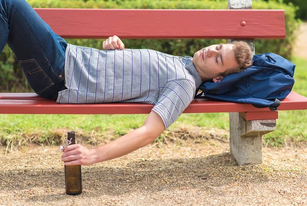 Junger Mann entspannt sich mit einer Flasche Bier auf einer Bank — Stockfoto