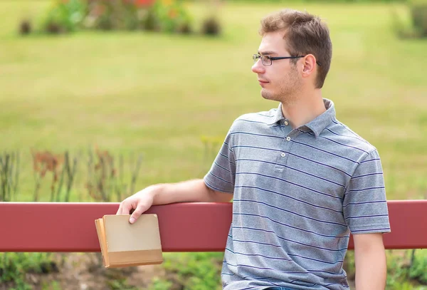 Joven sentado en un banco y sosteniendo un libro — Foto de Stock