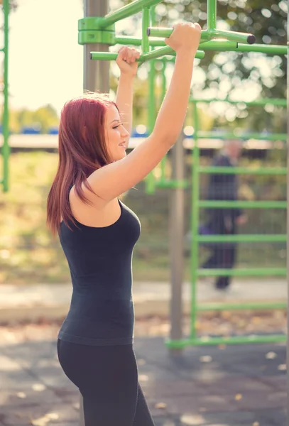 Beauty young woman chin ups in park — Stock Photo, Image