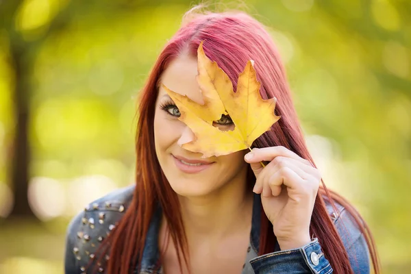 Woman sitting in the autumn park and playing with a leaf — Stock Photo, Image