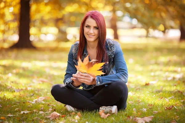 Woman sitting in the autumn park and playing with a leaf — Stock Photo, Image