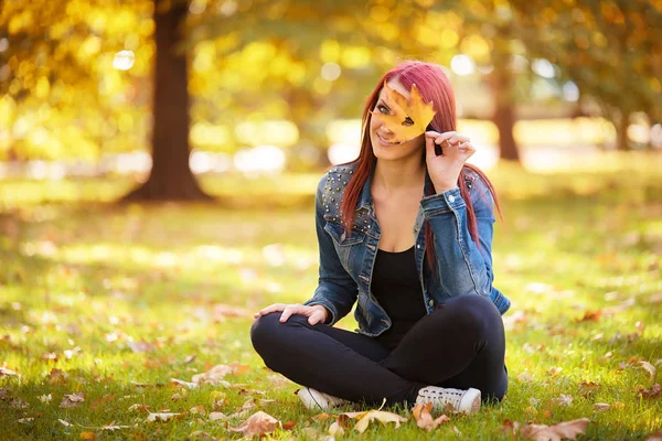 Sonbahar parkta oturan ve bir yaprak ile oynayan kadın — Stok fotoğraf