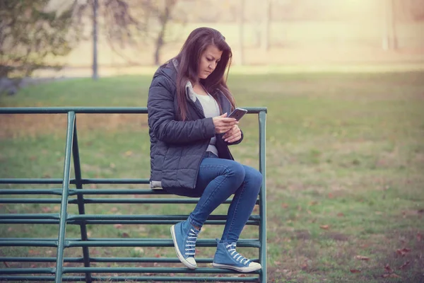 Woman sitting on a climbing frame and use her phone — Stock Photo, Image