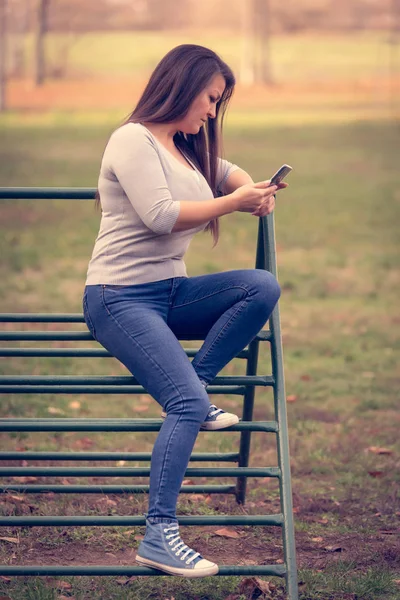 Mujer sentada en un marco de escalada y usar su teléfono — Foto de Stock