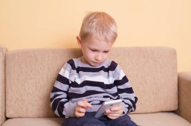 Genç sarışın çocuk akıllı telefon kullanıyor.