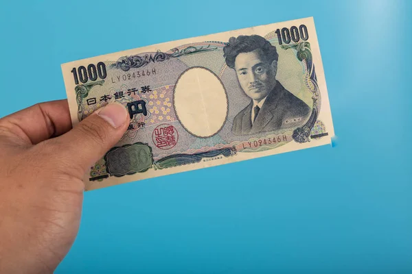 一只手拿着一千张蓝色背景的日圆钞票 — 图库照片