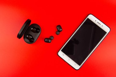 Kırmızı arkaplanda kablosuz bluetooth kulaklıklı akıllı telefon
