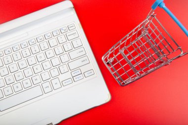 Kırmızı arkaplan çevrimiçi alışveriş konseptinde klavyeli boş market arabası