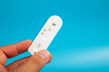 Mavi arka planda hamile test kiti tutan bir erkek eli.