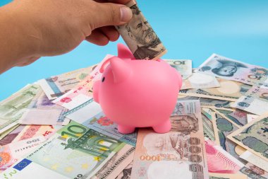 RMB YUAN banknotunu elinde tutan bir adam kumbaraya koydu. Masanın üstünde dünya banknotları koleksiyonu vardı. İş ve finans kavramı.