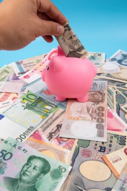 RMB YUAN banknotunu elinde tutan bir adam kumbaraya koydu. Masanın üstünde dünya banknotları koleksiyonu vardı. İş ve finans kavramı.