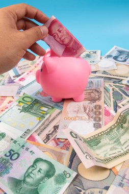 RMB YUAN banknotunu elinde tutan bir adam kumbaraya koydu. Masanın üstünde dünya banknotları koleksiyonu vardı. İş ve finans kavramı.