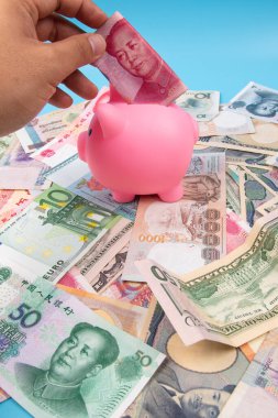 RMB YUAN banknotunu elinde tutan bir adam kumbaraya koydu. Masanın üstünde dünya banknotları koleksiyonu vardı. İş ve finans kavramı.