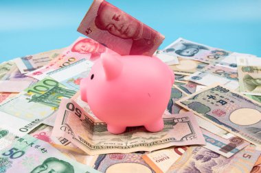 RMB YUAN banknotunu elinde tutan bir adam kumbaraya koydu. Masanın üstünde dünya banknotları koleksiyonu vardı. İş ve finans kavramı.