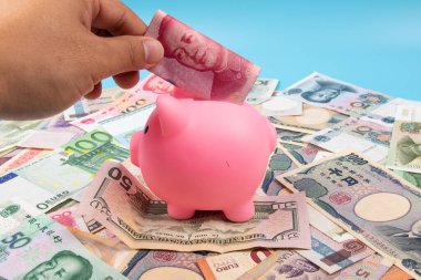 RMB YUAN banknotunu elinde tutan bir adam kumbaraya koydu. Masanın üstünde dünya banknotları koleksiyonu vardı. İş ve finans kavramı.