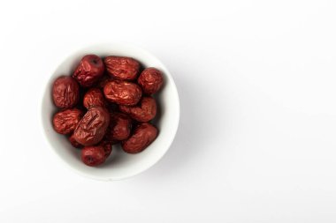 Beyaz arkaplanda bir kase kurutulmuş kırmızı hurma meyvesi..