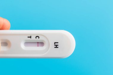 Mavi arka planda hamile test kiti tutan bir erkek eli.