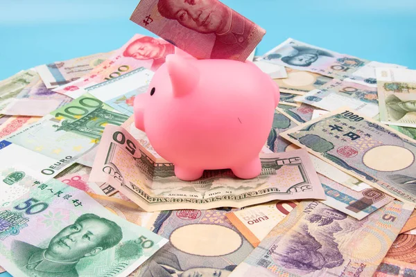 RMB YUAN banknotunu elinde tutan bir adam kumbaraya koydu. Masanın üstünde dünya banknotları koleksiyonu vardı. İş ve finans kavramı.