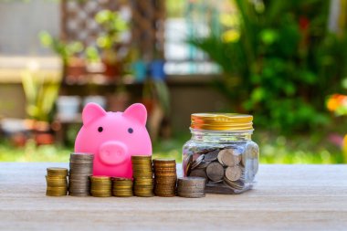 Domuz kumbarası, bozuk paralar ve doğanın bulanık arka planında saat. Para biriktirme kavramı.