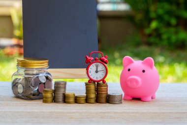 Domuz kumbarası, bozuk paralar ve doğanın bulanık arka planında saat. Para biriktirme kavramı.