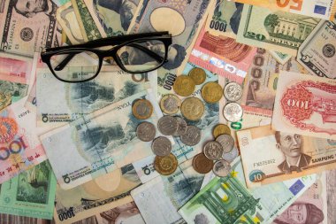 Dünya çapında banknotları olan gözlük, farklı ülkelerin arka planında yer alıyor. ABD Doları, Çin Yuanı, Japon Yen, Euro, Kore kazandı, Tayland bahtı. Forex veya küresel mali ekonomi kavramı.