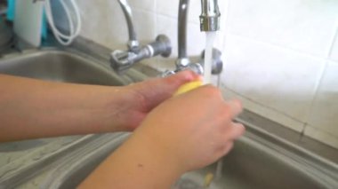 Kadın mutfak lavabosunda kırmızı elma yıkıyor.