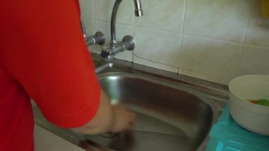Ev işi yapan bir adam lavaboda bulaşık yıkıyor.