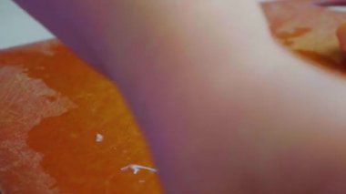 Kadının elleri bıçakla ince bir tavuk filetosunu kesiyor. Masada tavuk eti.