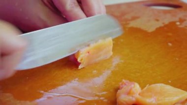 Kadının elleri bıçakla ince bir tavuk filetosunu kesiyor. Masada tavuk eti.